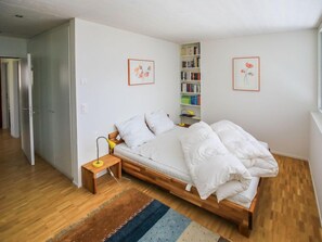 Un dormitorio con una cama de madera, una mesita de noche con lámpara, una estantería y dos cuadros en la pared.