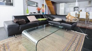Una sala de estar moderna con un sofá de cuero negro, una mesa de centro de vidrio y una alfombra estampada.