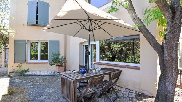 Een terras met een houten tafel en stoelen, een parasol en een bloempot.