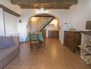 A cozy kitchen with a dining area, wooden beams, a staircase, and a fireplace.