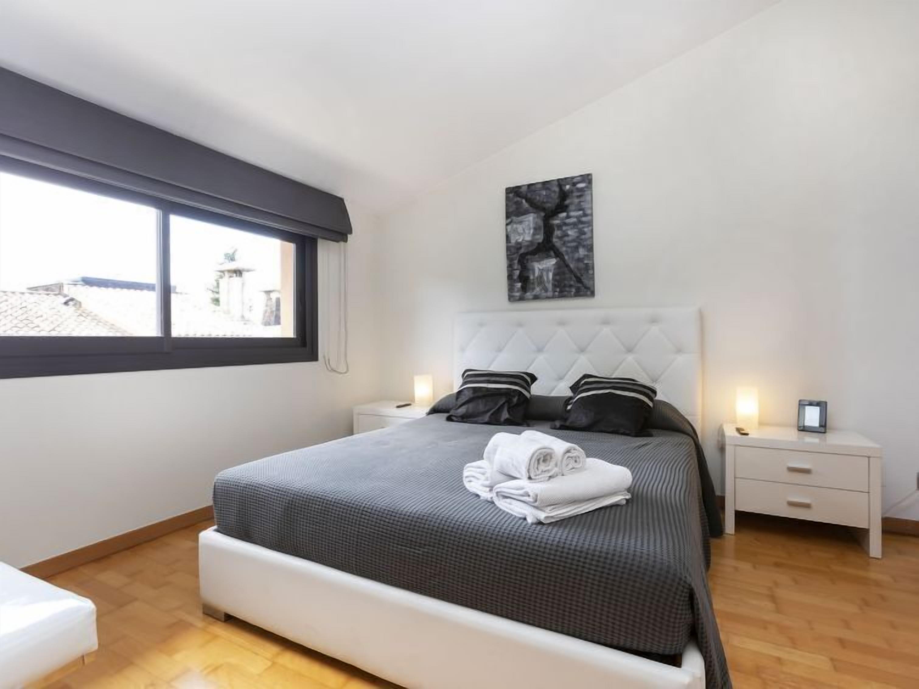 Un dormitori modern amb un llit gran, nits blanques, una finestra amb vistes i una obra d'art a la paret.