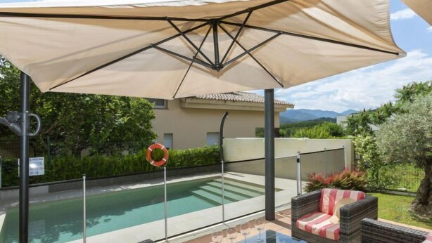 Area piscina con mobili in vimini, un tavolo in vetro e un ombrellone grande.