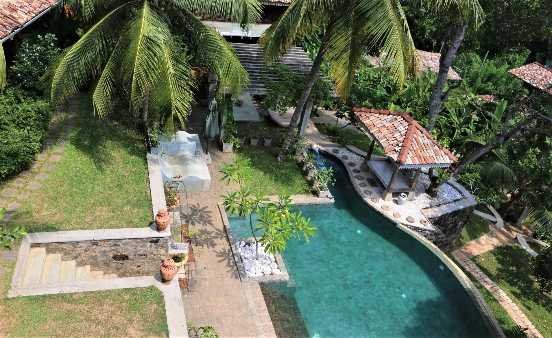 A pool area with a clear blue pool, surrounded by palm trees and a small gazebo.