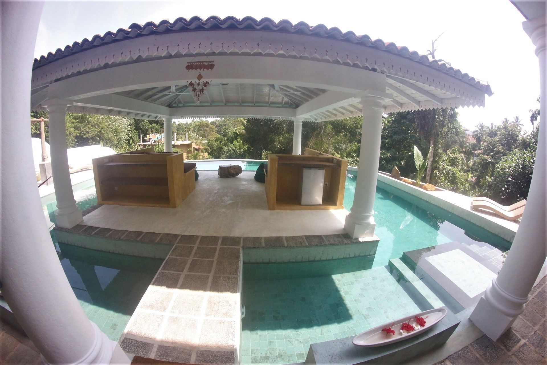 A covered outdoor area with a pool, wooden seating, and a small refrigerator.
