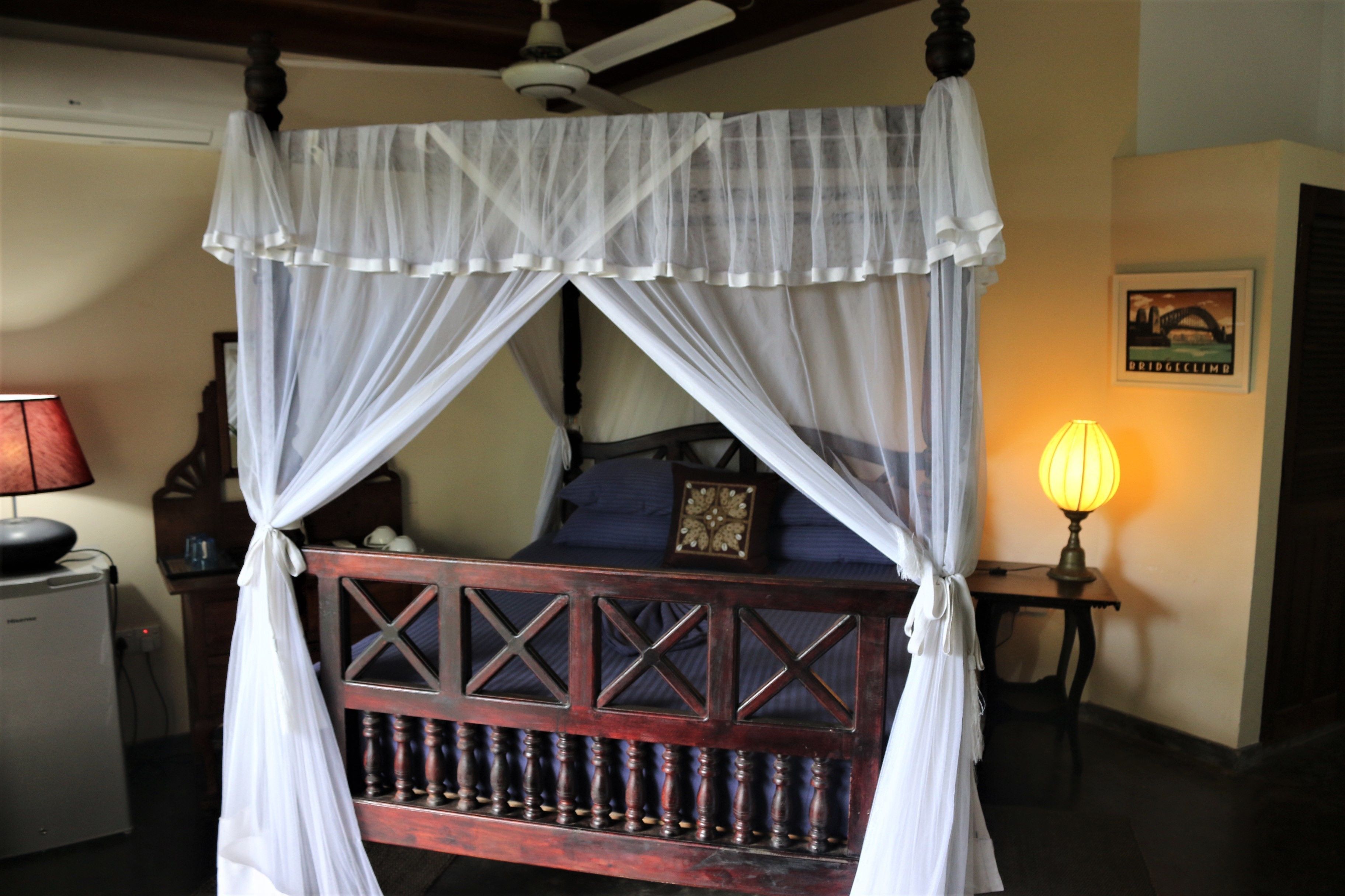 A four-poster canopy bed with a wooden frame and white drapes.
