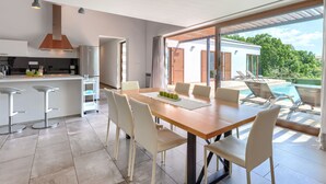 Cozinha moderna com ilha central, sala de jantar com mesa e cadeiras de madeira, e vista para uma piscina e área externa.