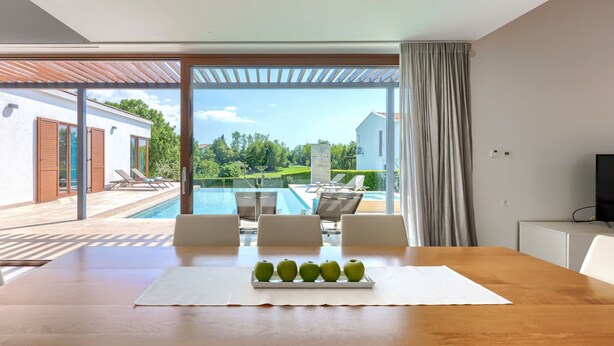 Uma zona de refeições moderna com mesa de madeira, cadeiras brancas e um tabuleiro com maçãs verdes.