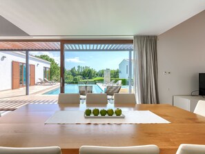 A modern dining area with a wooden table, white chairs, and a tray of green apples. - Luna Bianca by Interhome (Sveti Petar u Šumi)