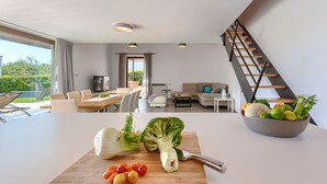 Uma sala de estar moderna com área de jantar, escada e bancada na cozinha com legumes frescos.
