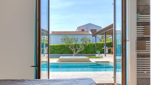 Quarto com uma grande porta de correr de vidro que dá para uma área de piscina, uma cama e vista para uma casa e um jardim.