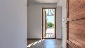 Corredor com porta de madeira que dá para área externa com vista para árvores e um edifício.