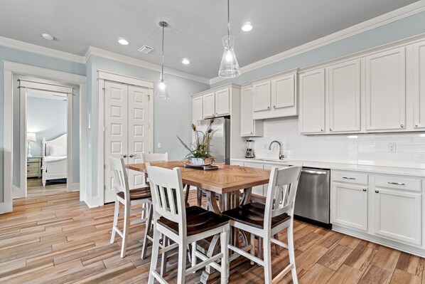 A modern kitchen with white cabinets, a wooden dining table, and a dishwasher.