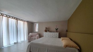 A bedroom with a large bed, a nightstand, a dresser, a chair, and a window with curtains.