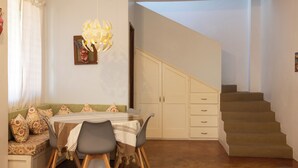 A dining area with a table, chairs, and a bench. There is a staircase leading to an upper level.