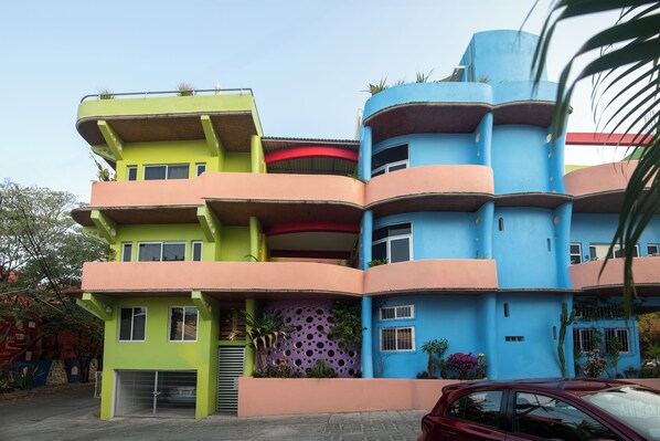 A multi-story building with balconies, a garage, and a car parked in front.