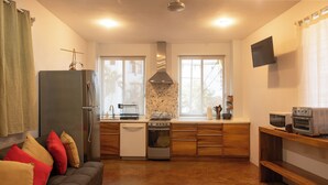 A compact kitchen with a built-in oven, a microwave, and a stove. There is a wooden dining table and a sofa with cushions.