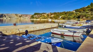 A marina with several boats docked, a stone wall, and a hillside with vegetation and buildings in the background. - Apartment Ivan by Interhome (Maslenica)