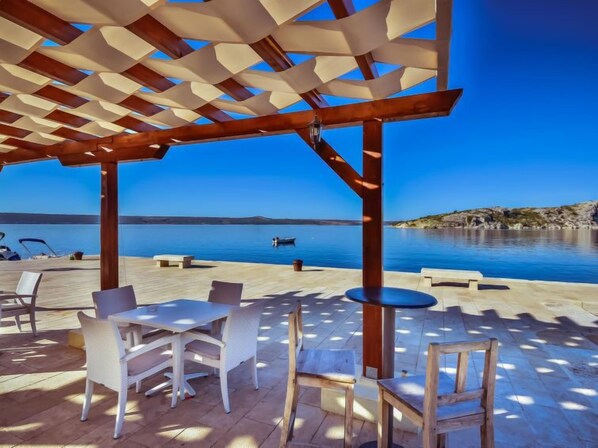 Terraza exterior con pérgola, asientos y vista al mar.