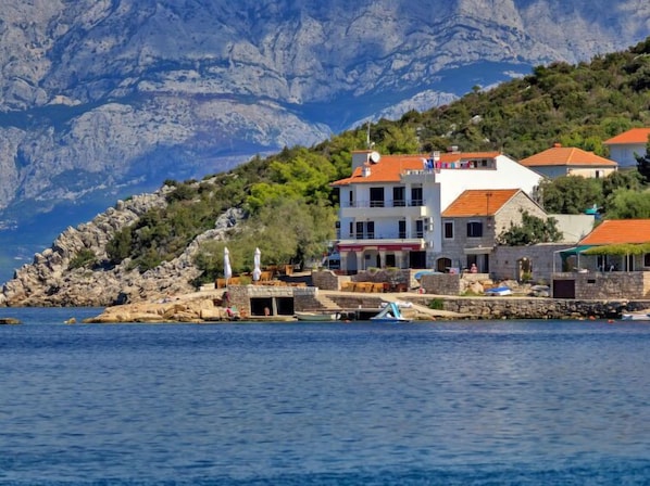 A coastal building with a stone facade, multiple balconies, and a red-tiled roof.