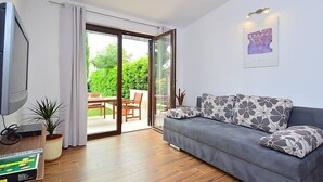 Un salon avec un canapé gris, un téléviseur à écran plat, une table en bois et une porte-fenêtre coulissante donnant sur une terrasse.