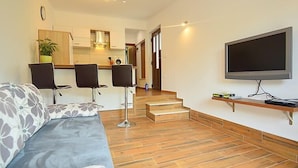 Un salon moderne comprenant un canapé, deux tabourets de bar, un téléviseur et un escalier menant à la cuisine.