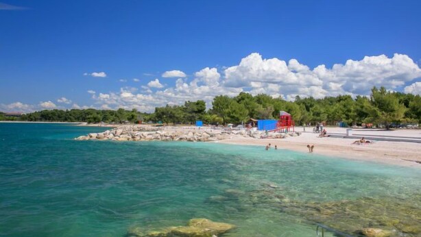 Une plage avec une eau turquoise et limpide, un rivage sablonneux et une structure rouge.