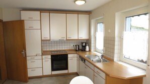 A compact kitchen with white cabinets, a built-in oven, a dishwasher, and a window providing natural light. - Haus Irmgard by Interhome (Blankenrath)