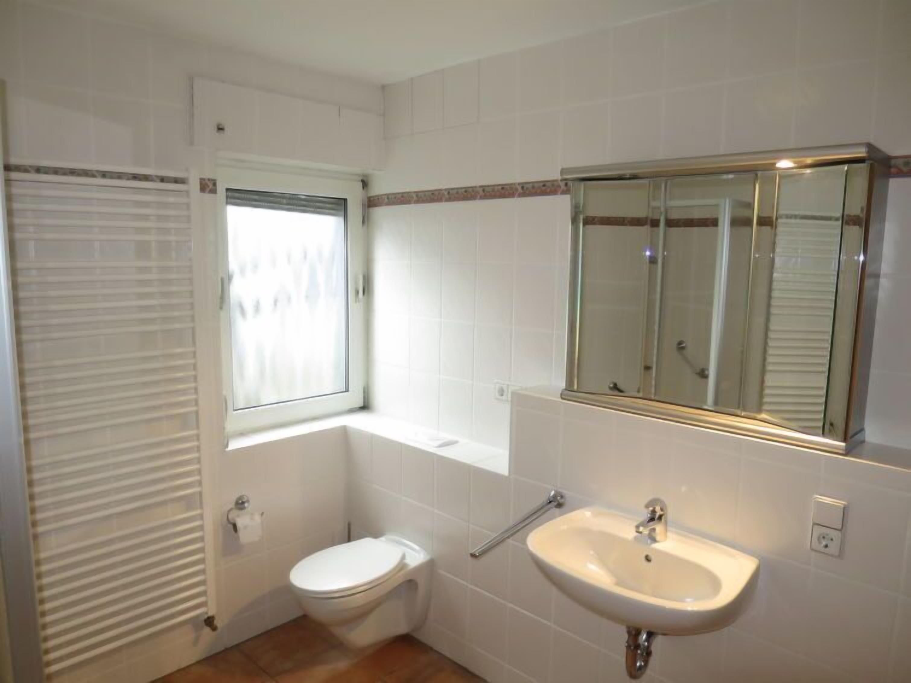 A small bathroom with a toilet, sink, and a window with blinds.