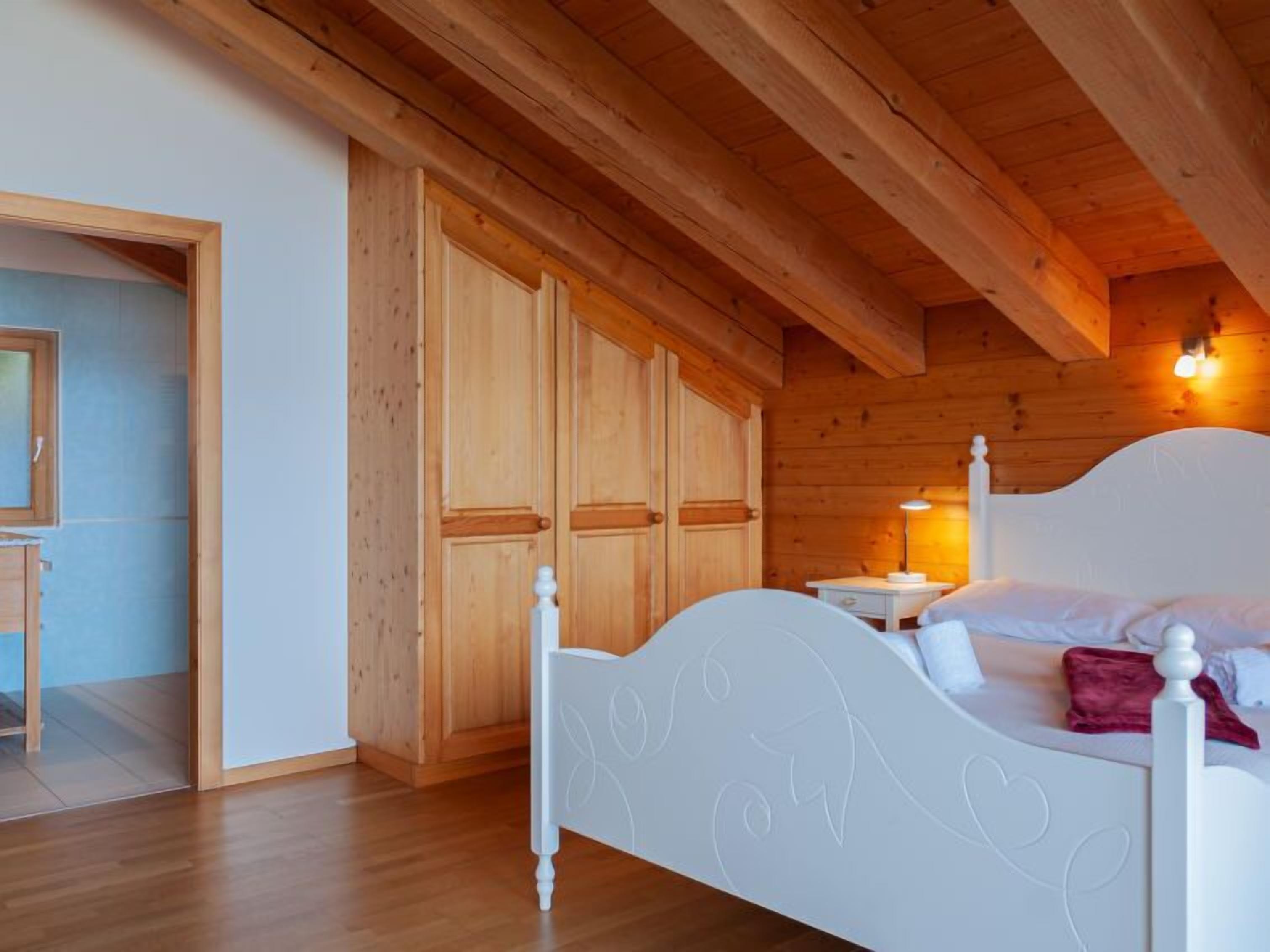 Een slaapkamer met een houten plafond, een wit bed met een decoratieve hoofdbord en een houten garderobe.