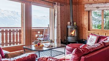 Une pièce chaleureuse avec un canapé en cuir, une table en verre sur laquelle sont disposés des fruits, un intérieur de chalet en bois et un poêle à bois.