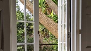 Uma porta que dá para um pátio com uma cadeira de madeira e uma estrutura de telhado de palha.