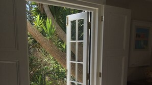 An open door leading to a patio with a concrete floor, surrounded by potted plants and a palm tree. - Little Treasure in Heart of Old Village Shanklin + Ferry Discount  (Shanklin)