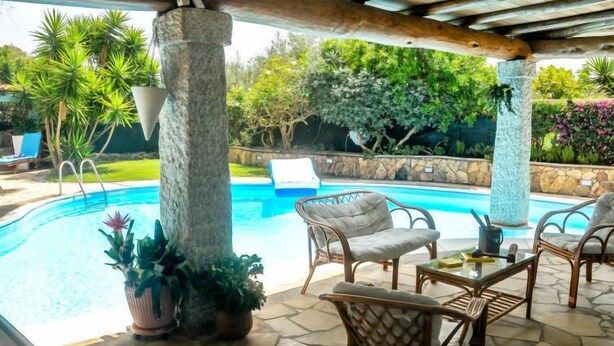 A covered outdoor area with a pool, wicker furniture, and potted plants.