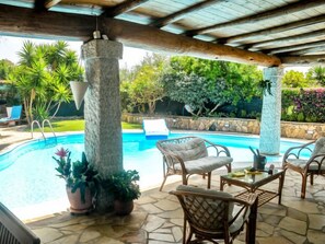 A covered outdoor area with a pool, wicker furniture, and potted plants. - Surphinia by Interhome (Bari Sardo)
