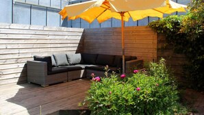 Une terrasse en bois avec un canapé gris et un parasol jaune.