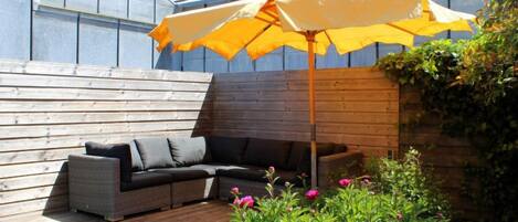 A wooden deck with a gray sofa and yellow umbrella.