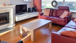 Un salon moderne avec une cheminée, un canapé en cuir rouge, une table basse en bois et un téléviseur posé sur un meuble blanc.