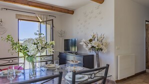 Un área de comedor con una mesa de vidrio, sillas y un televisor al fondo.