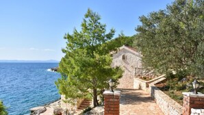 A stone pathway leading to a building with a red-tiled roof, surrounded by trees and overlooking the sea. - Villa Golubinka by Interhome (Hvar/Zastražišće)