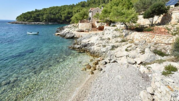 A coastal stone building with a staircase leading to a terrace, overlooking clear waters and a forested hillside. - Villa Golubinka by Interhome (Hvar/Zastražišće)