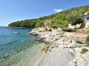 Eine Küstenlandschaft mit einem Steinhaus, klarem Wasser und einem Boot.