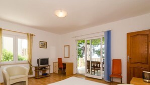 Ein Schlafzimmer mit einem Bett, einem Schreibtisch, einem Sessel, einem Fernseher und einer Glastür, die zu einem Außenbereich führt.