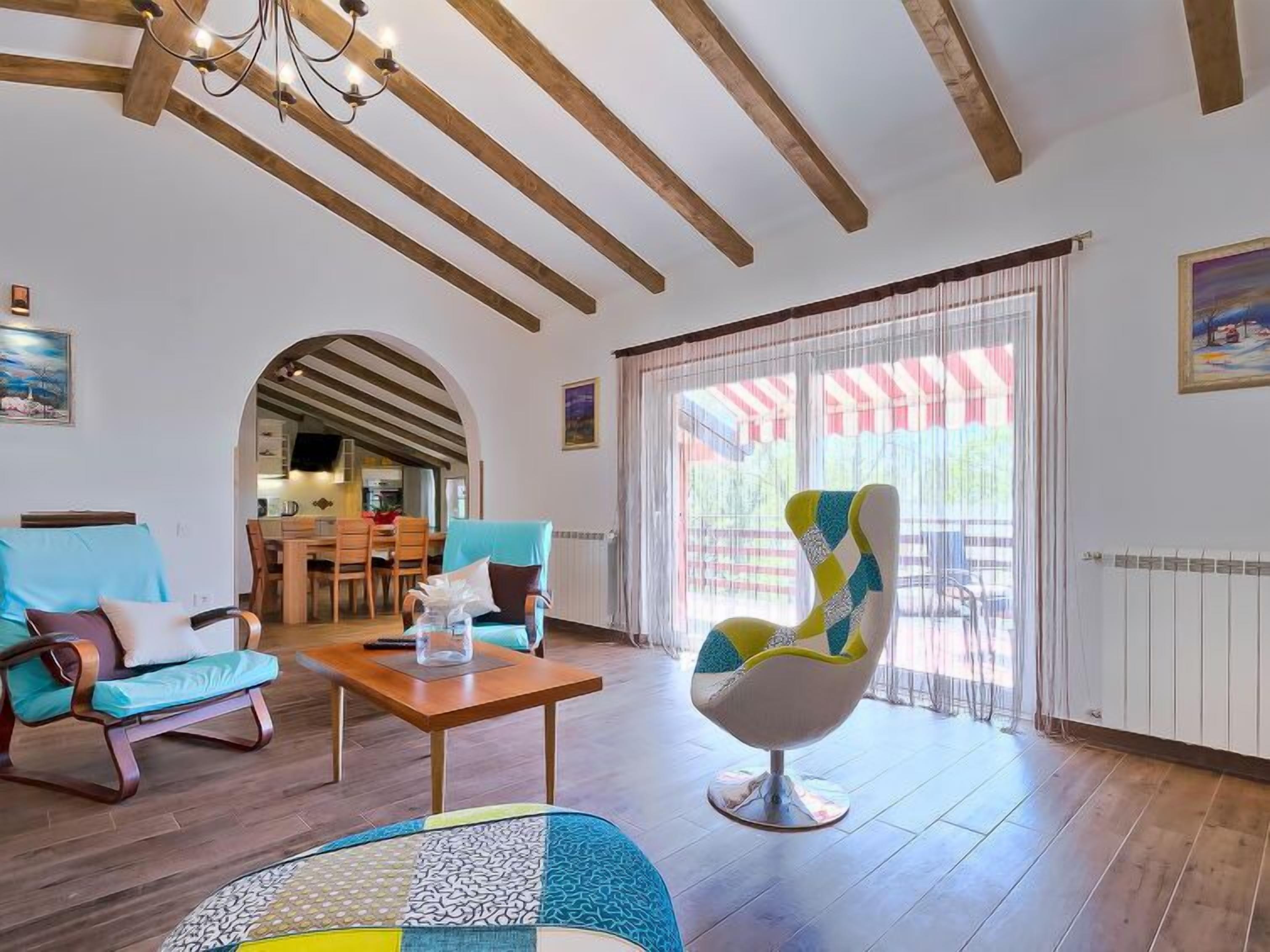 Amplia sala de estar con vigas de madera, una mesa de comedor, dos sillones y un sillón colorido.