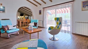 Amplia sala de estar con vigas de madera, una mesa de comedor, dos sillones y un sillón colorido.