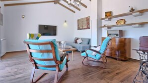 Amplia sala de estar con vigas de madera, un televisor, un sofá y dos sillones mecedores.