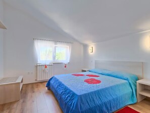 A bedroom with a large bed, a window with curtains, a bedside table, and a nightstand. - Apartment Majda by Interhome (Umag)