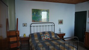 Un dormitorio con estructura de cama metálica, cómoda de madera, mesita de noche pequeña y un cuadro en la pared.