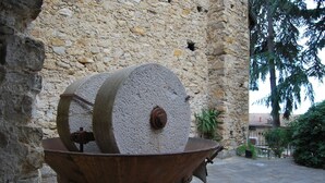 Una rueda de molino de piedra en un patio con un muro de piedra y árboles al fondo.