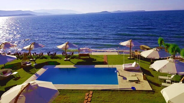 Ein Poolbereich mit Liegestühlen und Sonnenschirmen, umgeben von einer Rasenfläche mit Blick auf das Meer.
