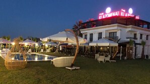 Ein Außenpoolbereich mit Liegestühlen und Sonnenschirmen, ein Gebäude mit leuchtendem Neonlicht und eine gut beleuchtete Terrasse.